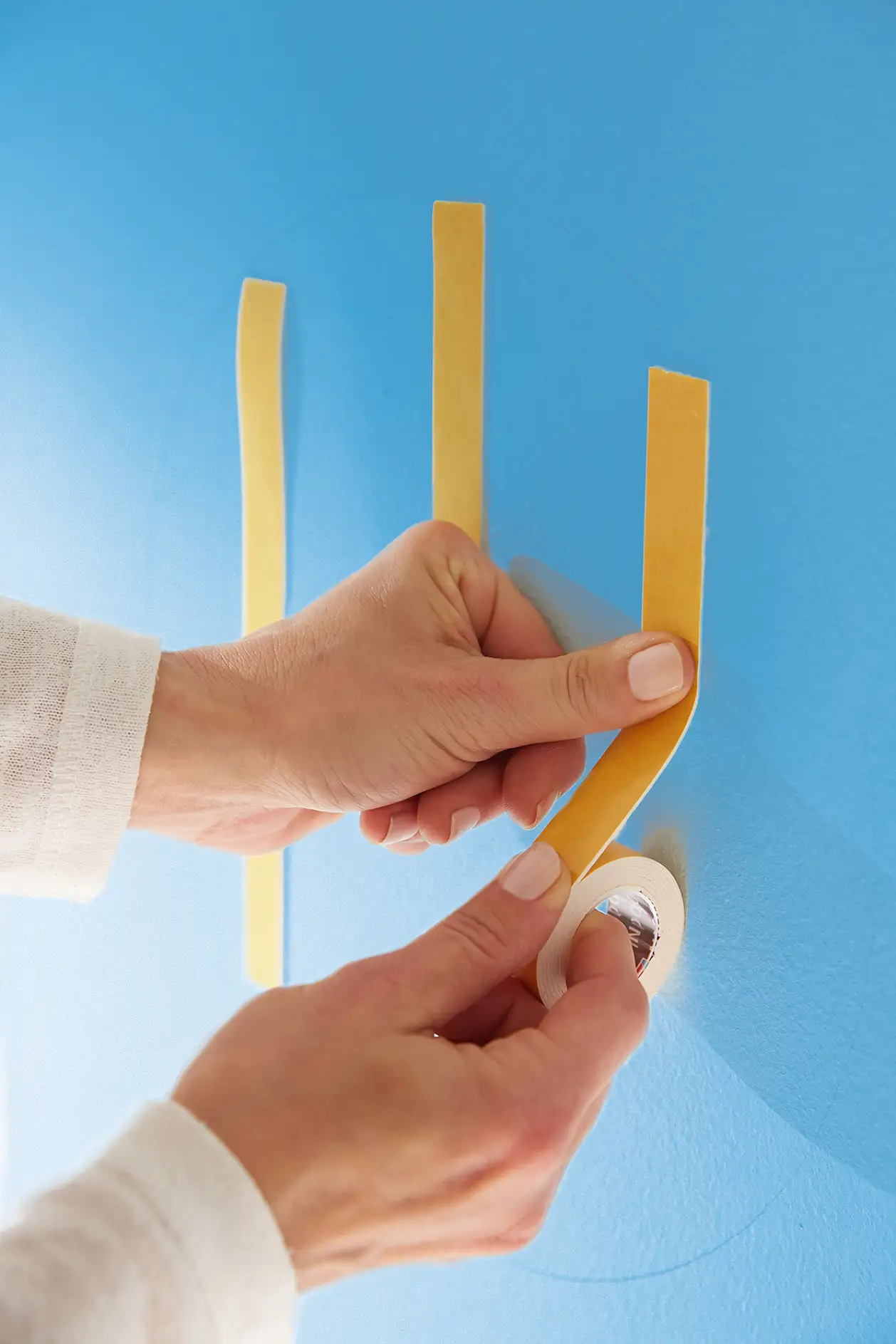 Odstraňte ze stěny prach a poté svisle nalepte dlouhé a krátké proužky pásky tesa® Powerbond INDOOR na vyznačená místa.