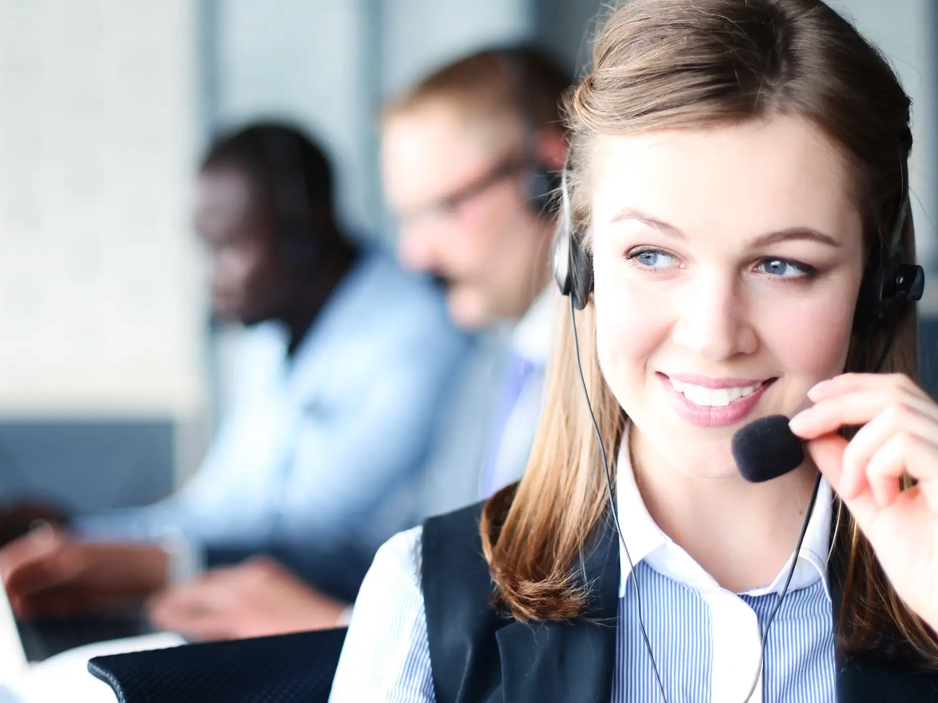 Portrét pracovnice call centra s týmem. Usměvavá pracovnice zákaznické podpory při práci.