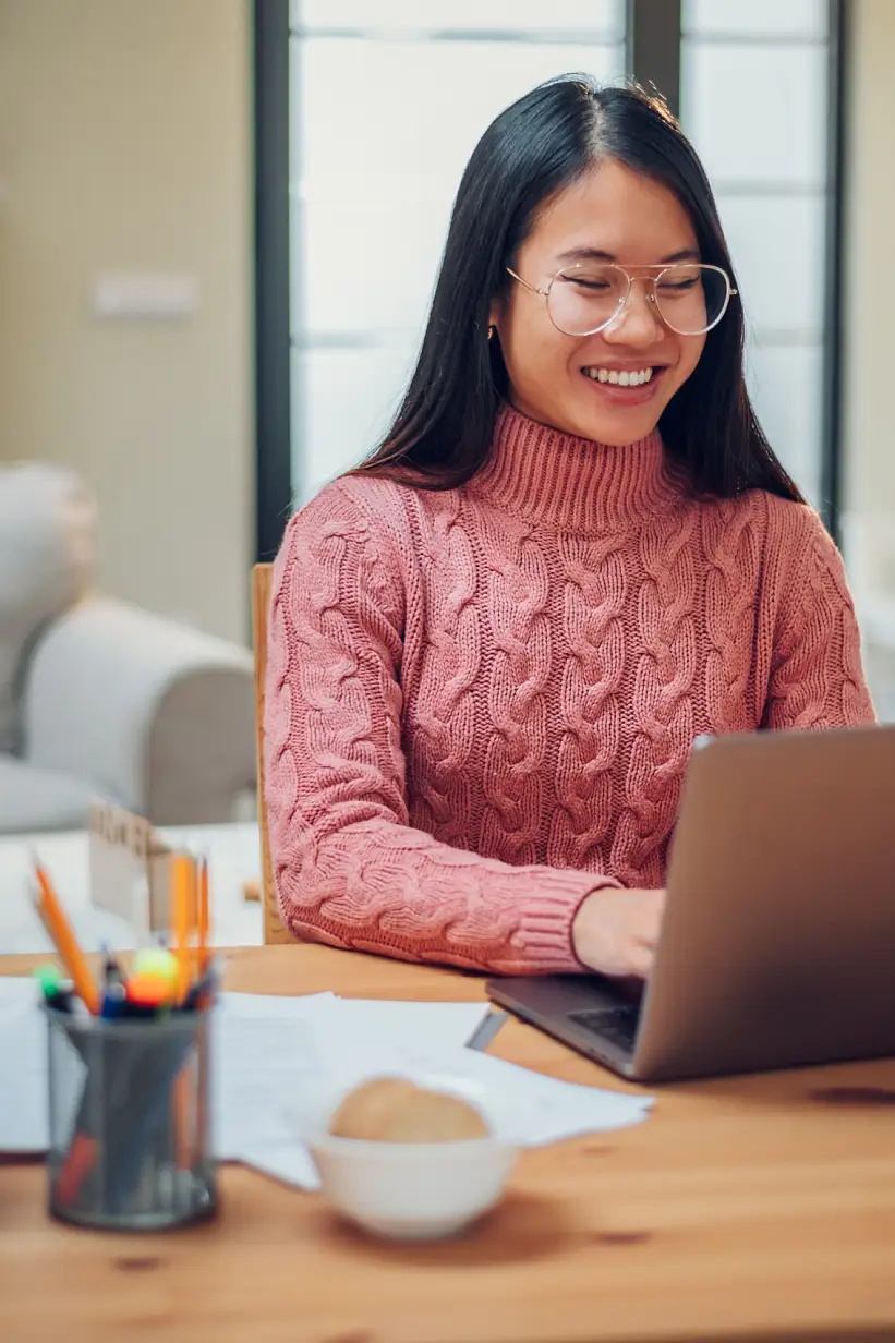 Young Vietnamese woman working in a home office and using a laptop. Flexible workspace and working time. Beautiful Asian business female or student typing an email or working on a project. Copy space.