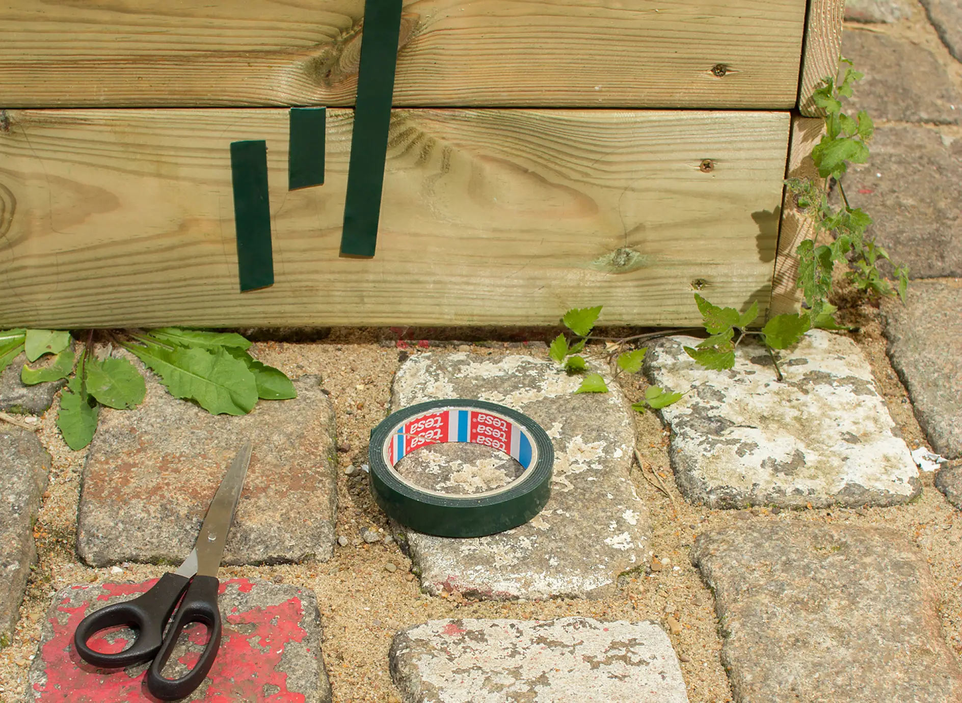 Scissors, tesa Powerbond® OUTDOOR adhesive tape and strips of tape applied to sandbox.