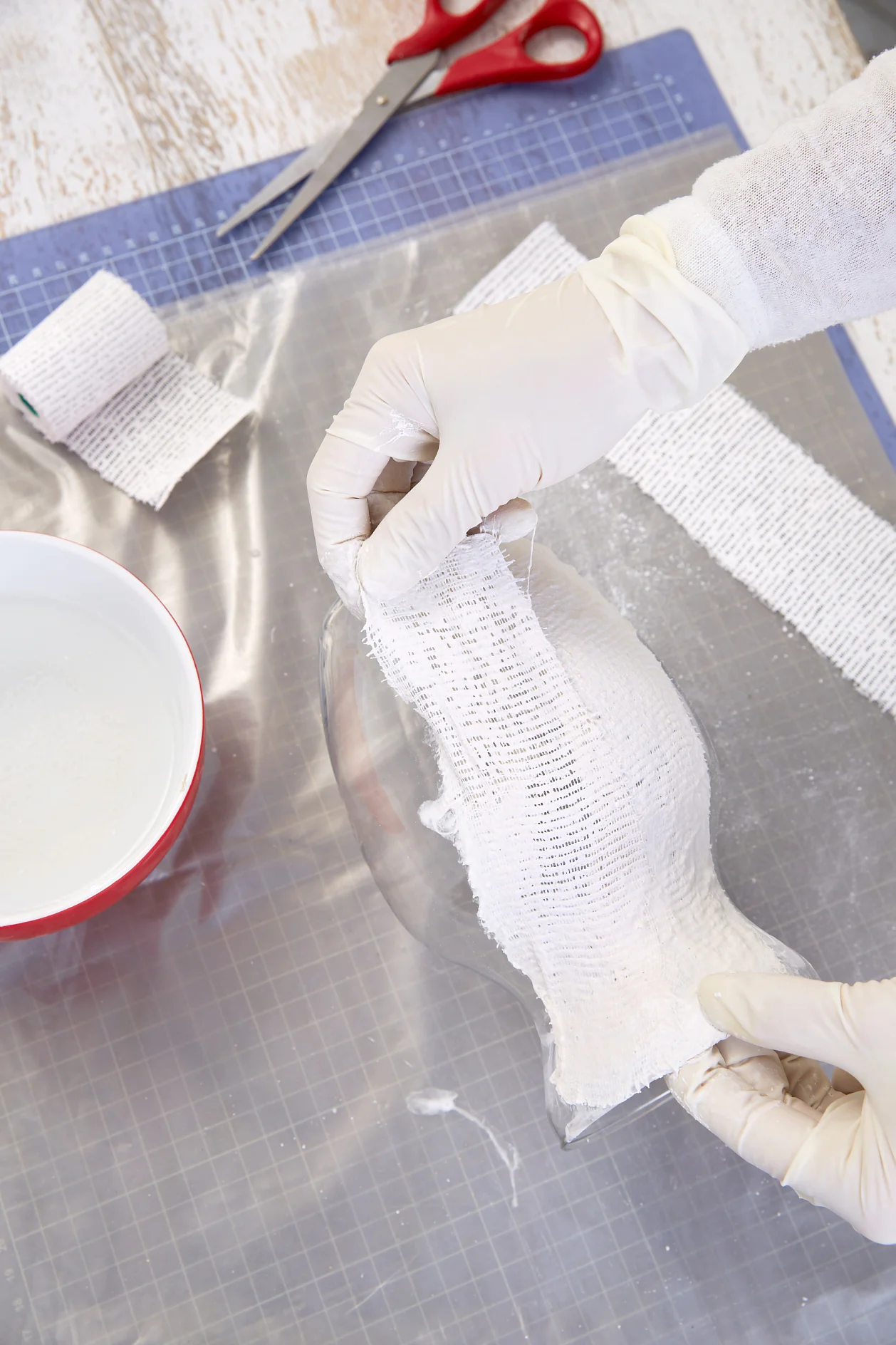 Now place one end of the wet plaster bandage even at the bottom of the vase; bend the remaining part on the top side into the opening. Repeat until the vase is fully covered with plaster bandages. Smoothen the surface. 
Allow the vase to dry.