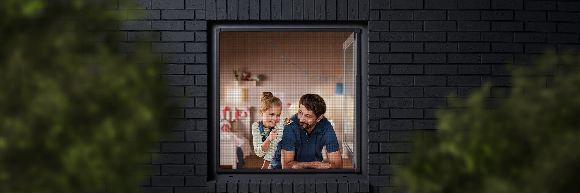 A man and a child are seen through a window, looking into a room decorated with colorful bunting. The building has dark brick walls, and the view is partially framed by blurred greenery. The man is wearing a blue shirt, and the child is sitting beside him. (This text has been generated by AI)