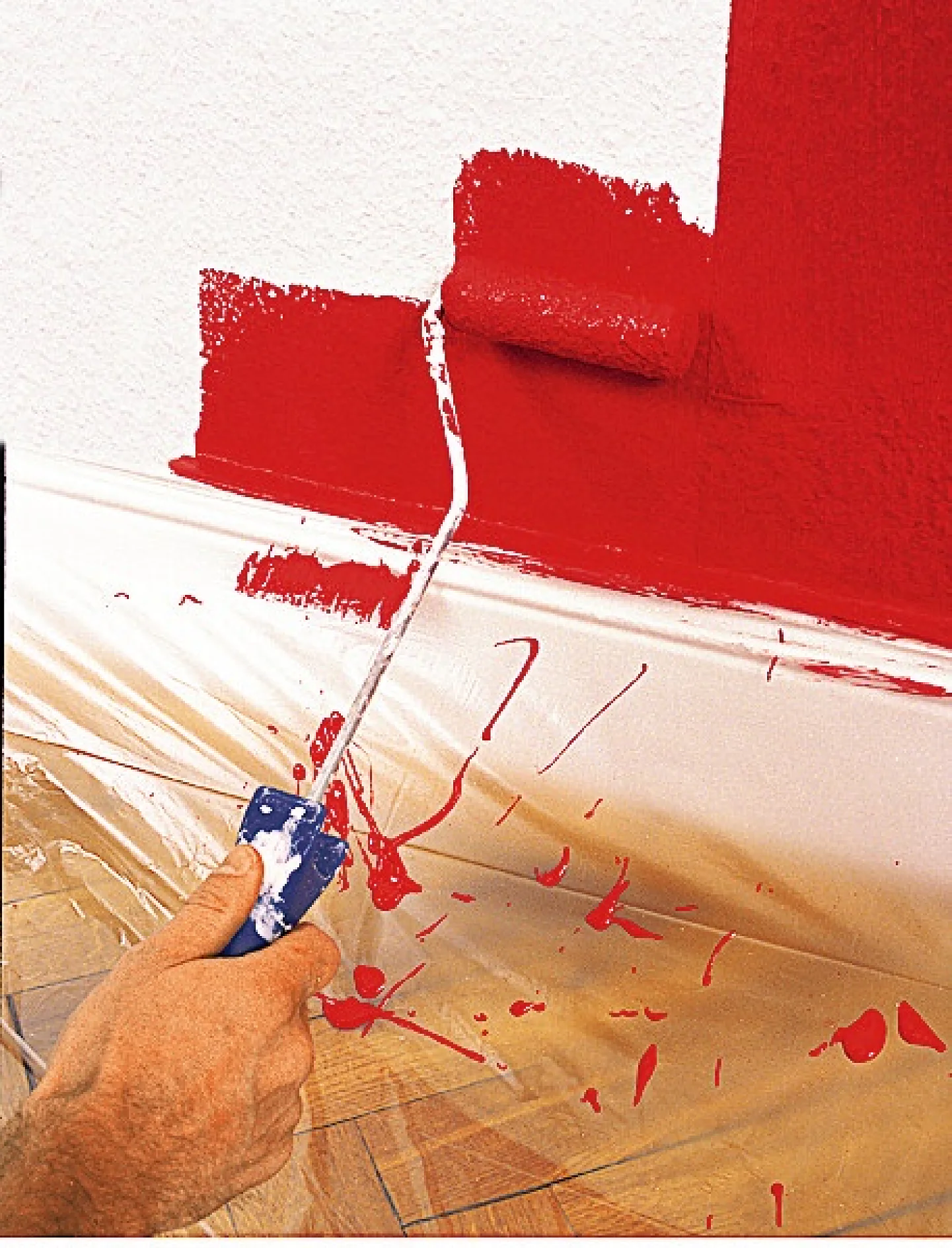 Ruka používá váleček k nanášení jasně červené barvy na bílou zeď. Podlaha je chráněna plastovou fólií a na fólii se rozstříklo trochu červené barvy. (This text has been generated by AI)