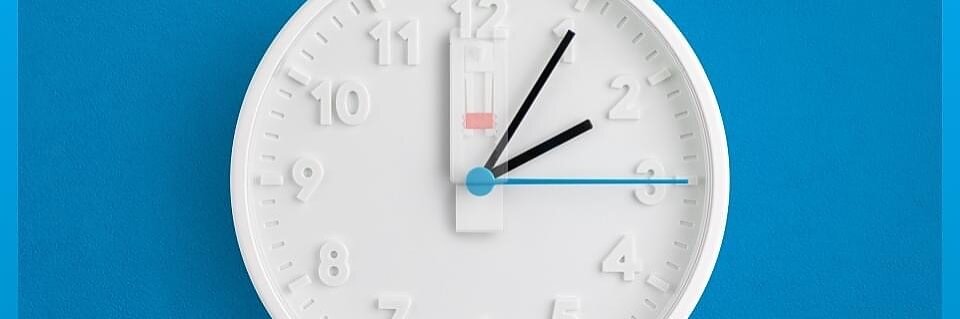 Bílé analogové hodiny s minimalistickým designem jsou umístěny na modrém pozadí. Ručičky hodin ukazují 2:14. Tři černé ručičky ukazují hodiny, minuty a sekundy, menší modrá ručička označuje jiné časové pásmo. Logo tesa tape je nad hodinami. (This text has been generated by AI)