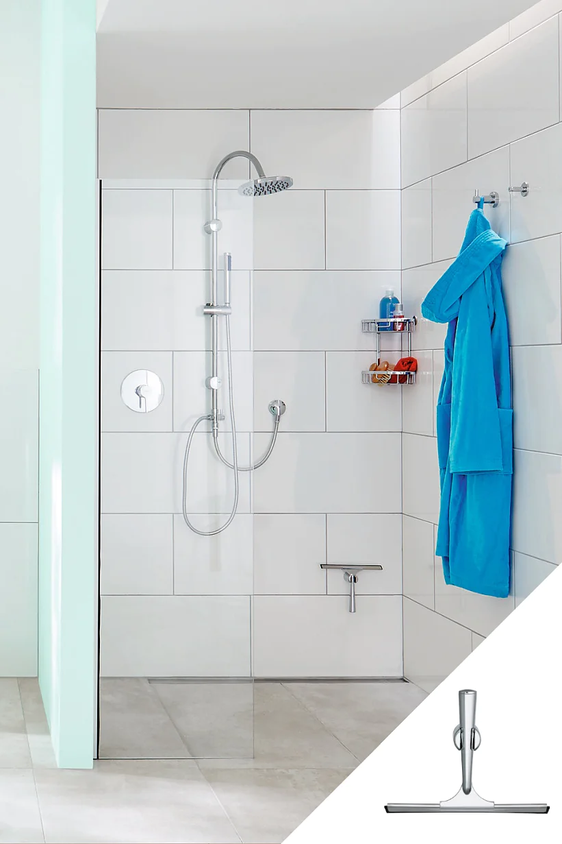 Moderní koupelna se sprchovým koutem se skleněnou stěnou, elegantní stříbrnou sprchovou hlavicí a příslušenstvím. Stěny jsou obloženy bílou dlažbou. Modrý župan visí na háčku, zajištěný páskou tesa, a toaletní potřeby jsou uloženy na kovové poličce. Ve spodním rohu je zobrazena stěrka okna. (This text has been generated by AI)