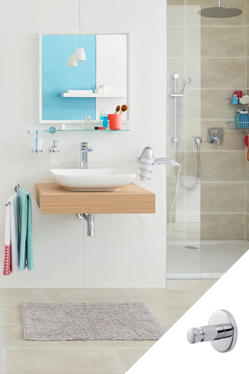 Moderní koupelna s plovoucím dřevěným umyvadlem a bílým umyvadlem, kulatým zrcadlem a sprchovým koutem s béžovými obklady. Na podlaze je světle šedá koupelnová předložka. Samostatná vložka zobrazuje chromový nástěnný háček zajištěný páskou tesa. Jsou vidět zavěšené ručníky a toaletní potřeby. (This text has been generated by AI)