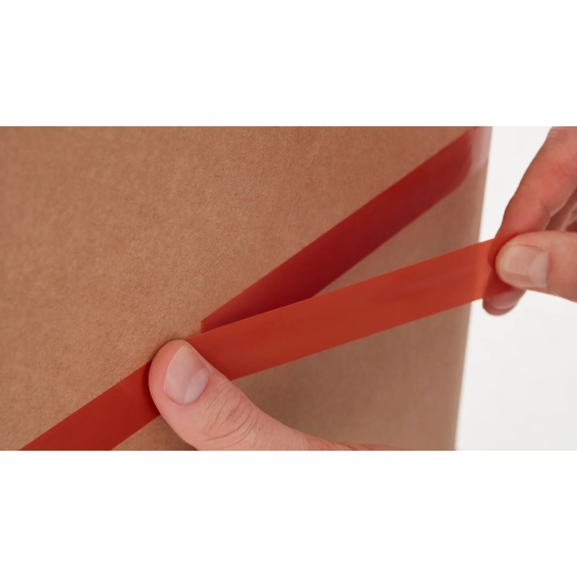 hands peeling red tesa tape from brown cardboard box in close-up, indoor setting (This text has been generated by AI)