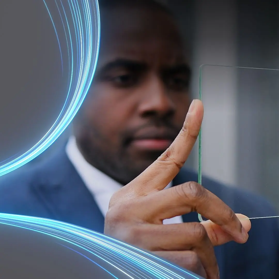 A person in a suit holds a transparent piece of tesa tape between their fingers, examining it closely. Blue glowing lines curve around the left side of the image, adding a futuristic element. (This text has been generated by AI)