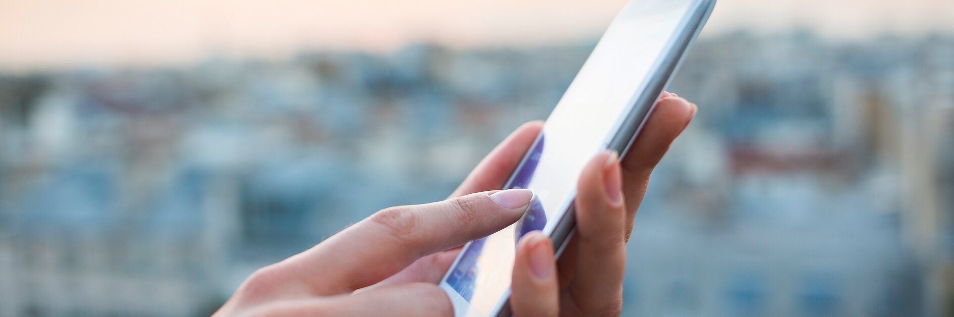 hands holding a smartphone outdoors with a blurred cityscape in the background during daylight