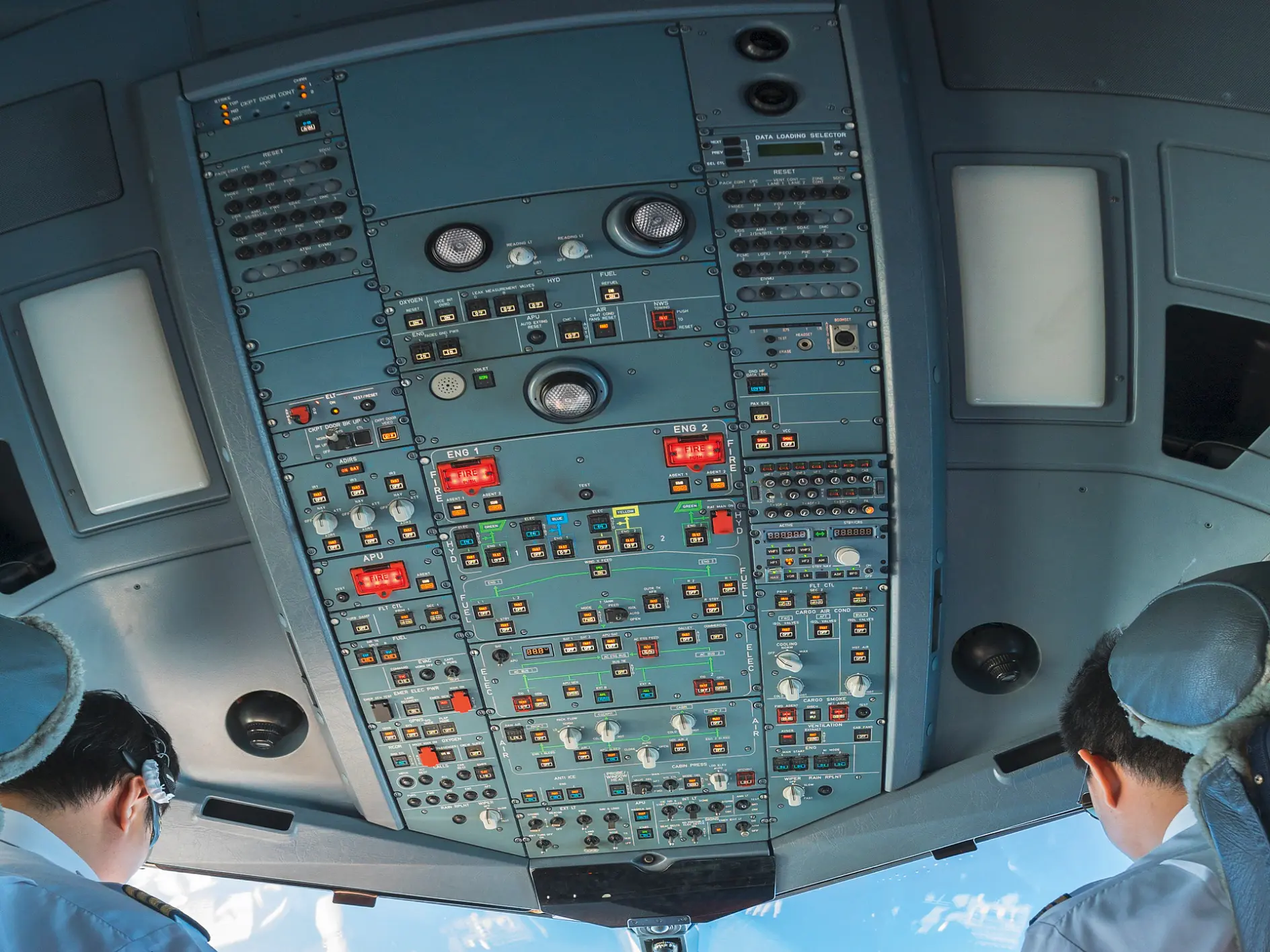 two pilots in uniform seated in an airplane cockpit operating controls with instrument panels and sky visible through windows (This text has been generated by AI)