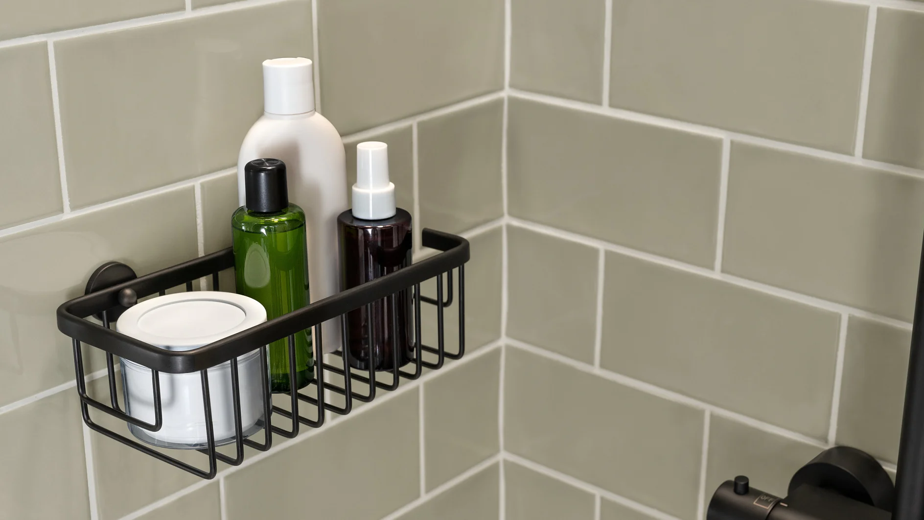 A shower caddy mounted on a tiled wall holds various toiletries, including a white bottle, a green bottle, a spray bottle, and a small white container. The tiles are a light grayish-green color, and the caddy is securely attached with tesa tape. (This text has been generated by AI)