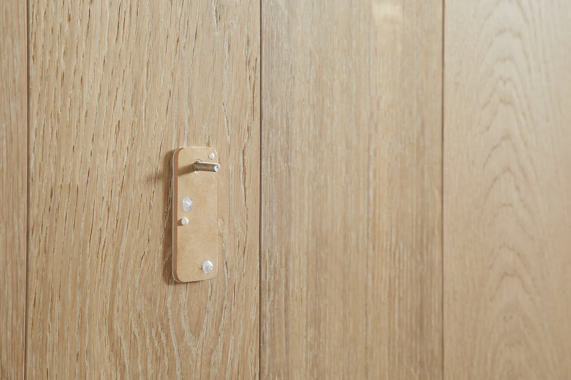 A light wood panel with a minimalist metal wall hook featuring a simple design. The hook is mounted vertically, with natural wood grain providing texture to the background, using tesa tape for secure attachment. (This text has been generated by AI)