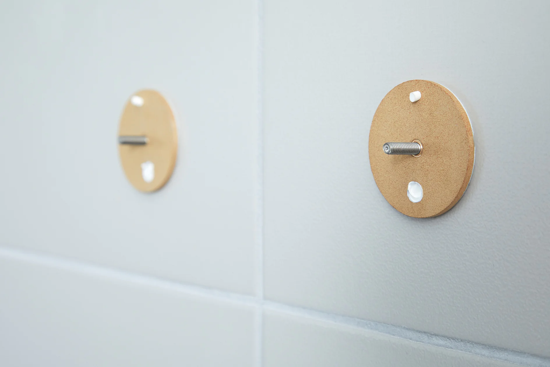 Two round cardboard templates with protruding metal rods are attached to a tiled wall. The templates are secured with small white spots of tesa tape, indicating an unfinished installation or mounting project. (This text has been generated by AI)