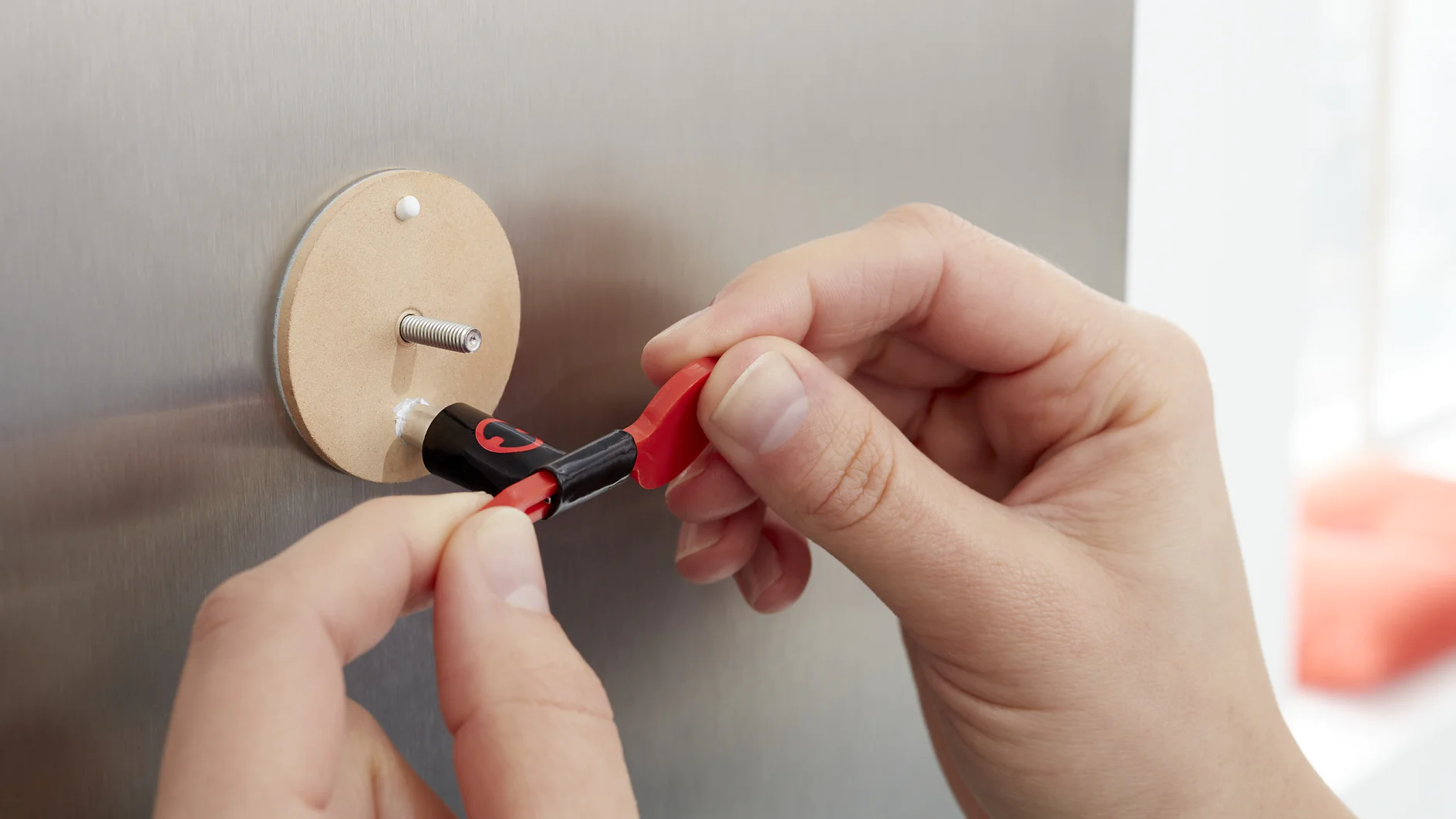 Two hands connect a red and black alligator clip to a metallic round contact on a gray surface. The clips feature insulation, and the setup appears to be part of an electrical or testing device, secured with tesa tape for stability. (This text has been generated by AI)