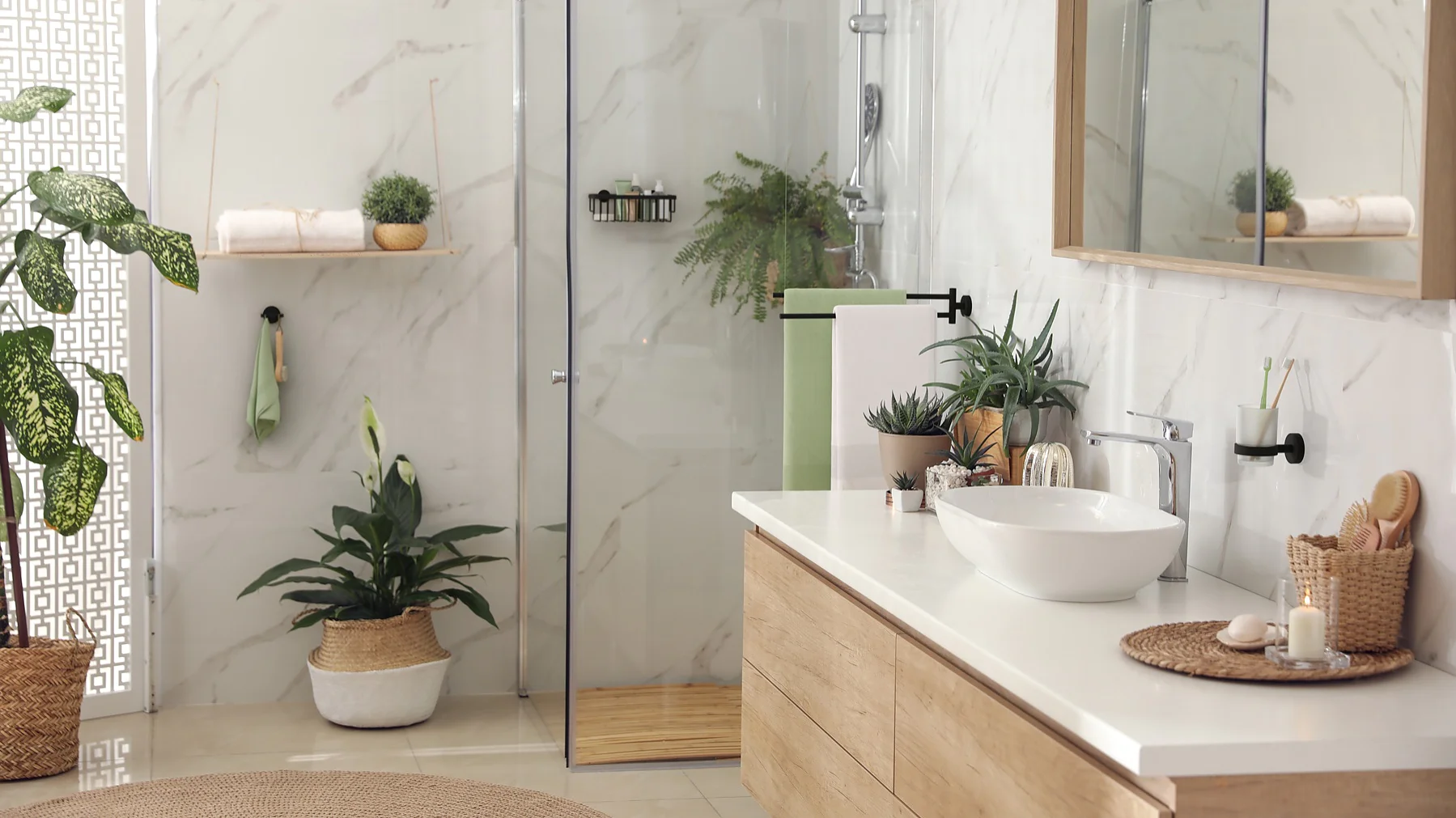 Modern bathroom with a glass shower, wood vanity, and white basin. White marble walls and multiple indoor plants enhance the decor. A mirror hangs above the sink, secured with tesa tape, and there are neatly arranged toiletries on the counter and shelves. (This text has been generated by AI)