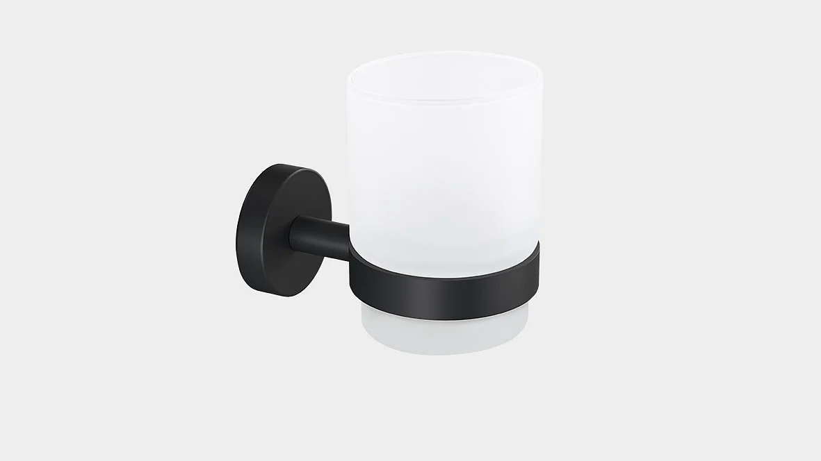 En matteret glaskop holdes af et sort metalbeslag, monteret på en væg. Beslaget har en rund bund og en cylindrisk holder, der understøtter koppen. Koppen er tom og baggrunden er almindelig hvid. (This text has been generated by AI)