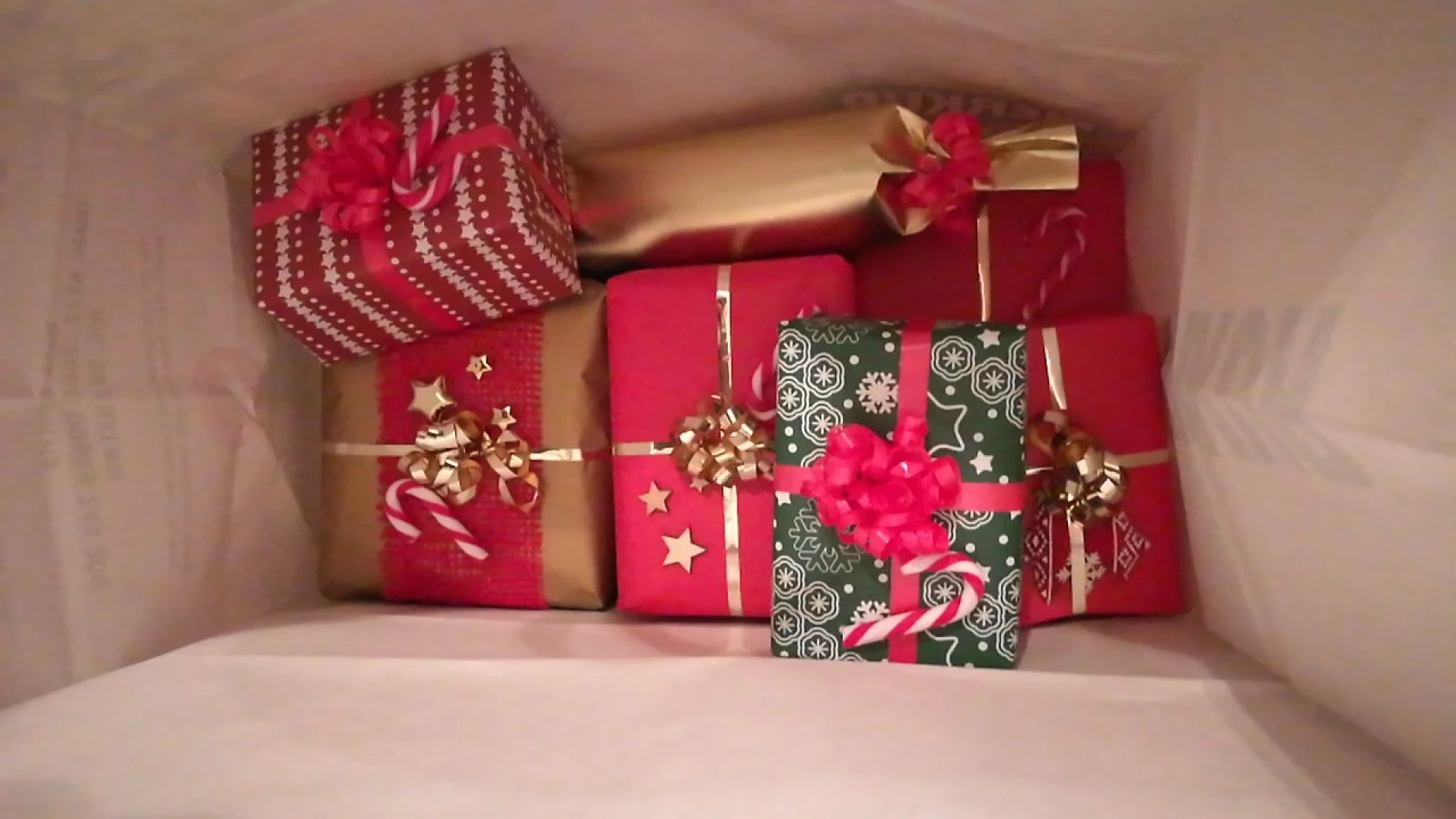 Eine Draufsicht auf mehrere hübsch verpackte Geschenke in einer Papiertüte. Die Geschenke sind in rotes, grünes und goldenes Papier mit festlichen Mustern eingewickelt und mit dekorativen Schleifen versehen. Alles ist mit Tesa-Klebeband befestigt. (This text has been generated by AI)