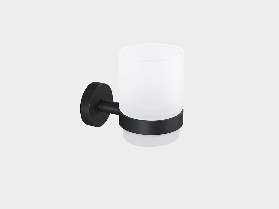 A frosted glass cup is held by a black metal bracket, mounted on a wall. The bracket has a round base and a cylindrical holder supporting the cup. The cup is empty and the background is plain white. (This text has been generated by AI)