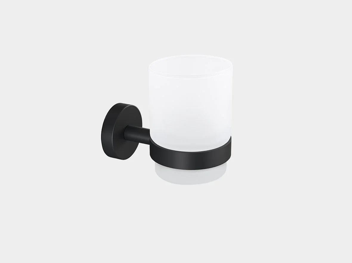 A frosted glass cup is held by a black metal bracket, mounted on a wall. The bracket has a round base and a cylindrical holder supporting the cup. The cup is empty and the background is plain white. (This text has been generated by AI)