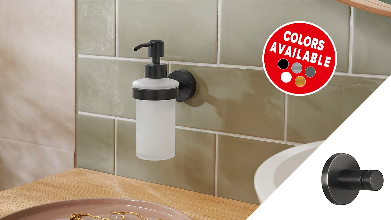 A wall-mounted soap dispenser with a frosted bottle and black pump is attached to a light green tiled wall using tesa tape. A circular decal shows various available colors: red, white, gray, beige, and black. A wooden counter is in the foreground. (This text has been generated by AI)