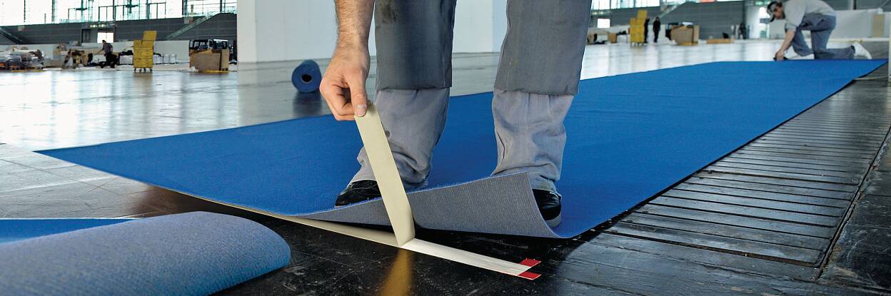 Professioneller Handwerker verwendet doppelseitiges Verlegeband zum Fixieren eines Teppichs.