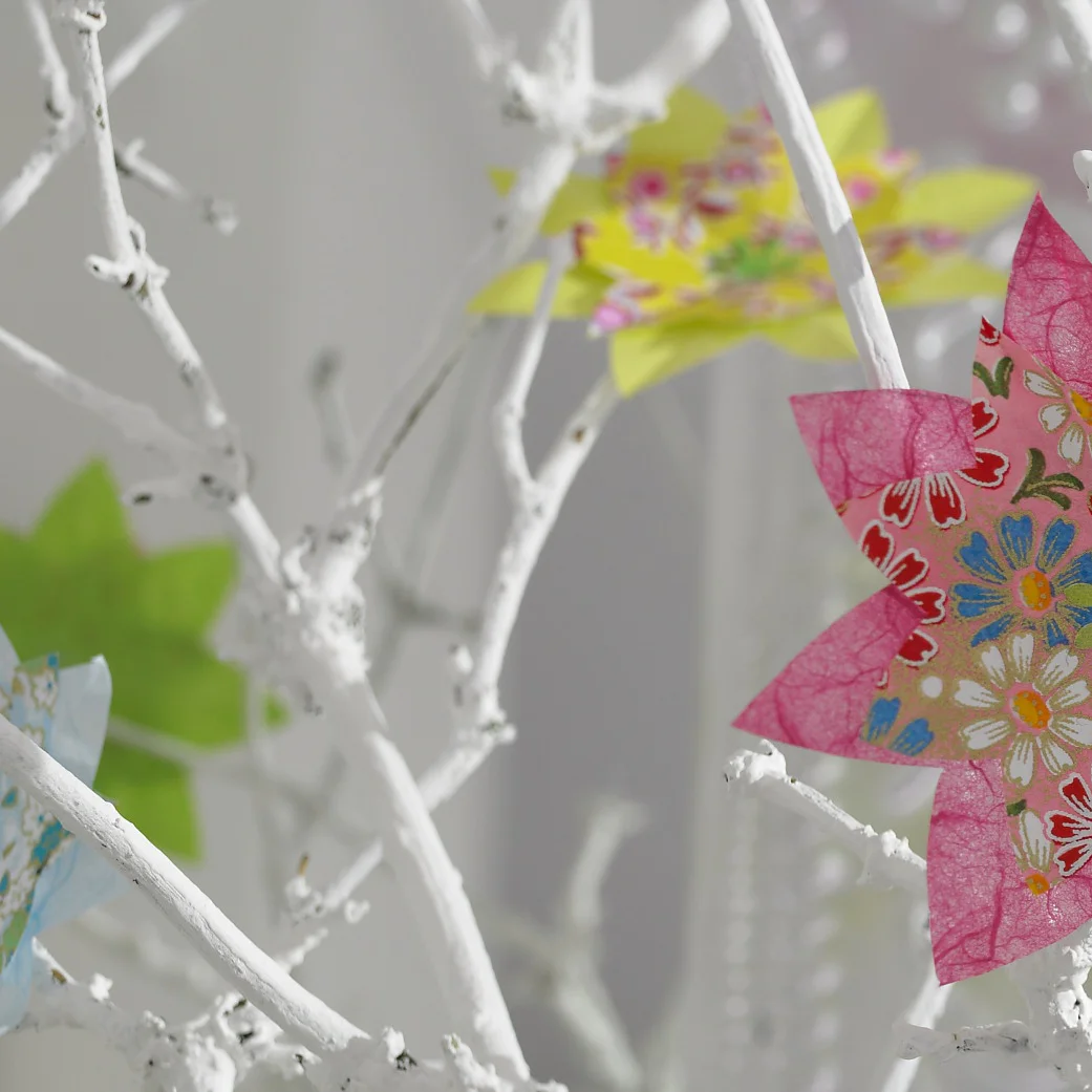 Bunte Blumen im Origami-Stil lassen die weißen Zweige aufblühen.