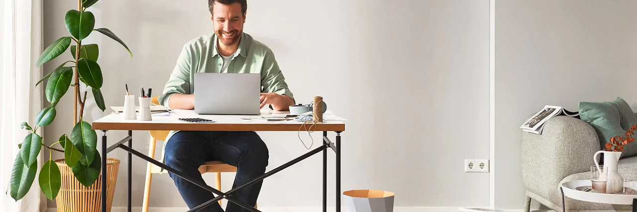 Mit tesa® Ordnung ins Wohnzimmer bringen! Mann sitzt an einem Schreibtisch im Wohnzimmer und genießt die Ordnung im Wohnzimmer