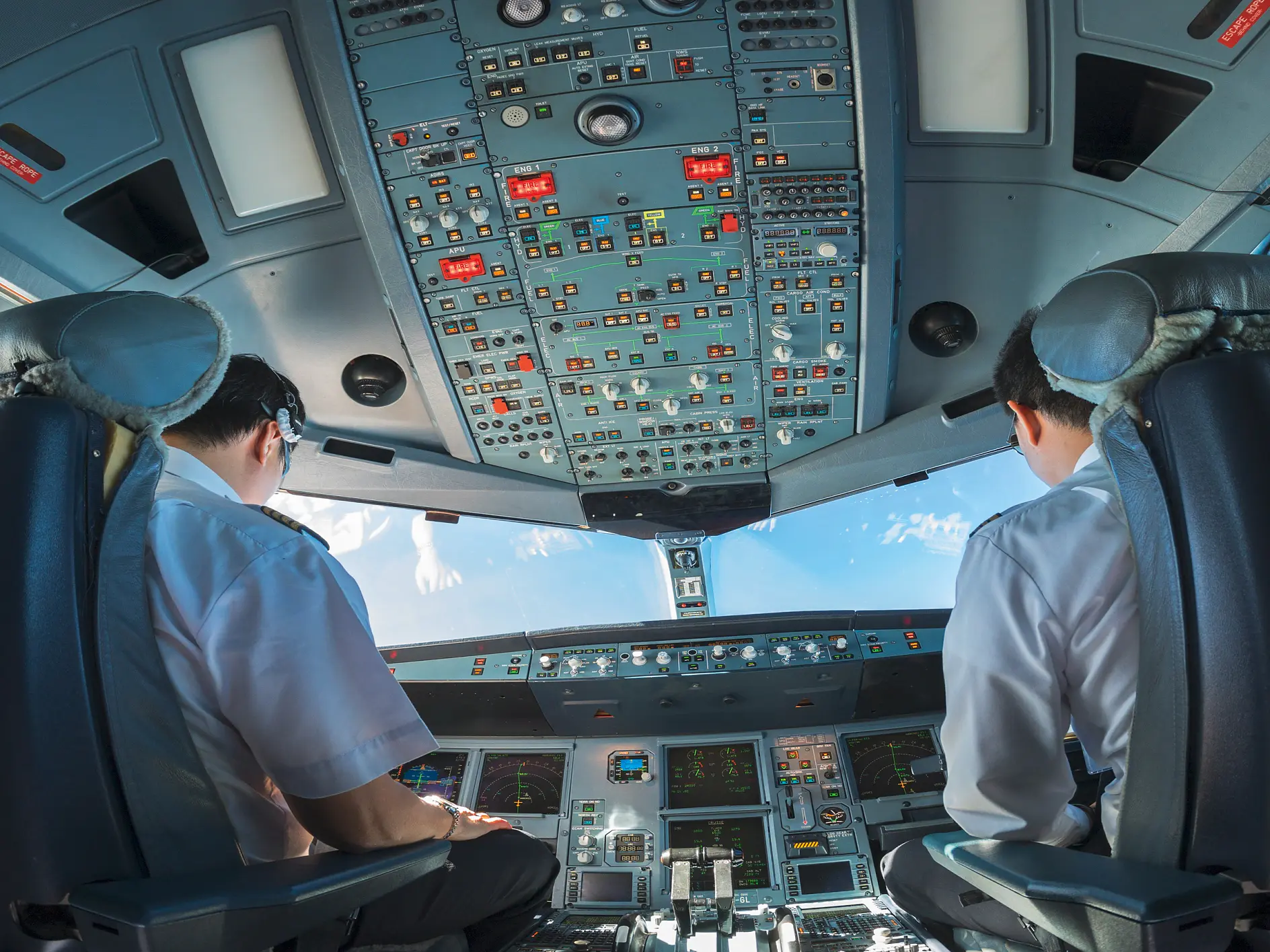 two pilots in uniform seated in an airplane cockpit operating controls with instrument panels and sky visible through windows (This text has been generated by AI)