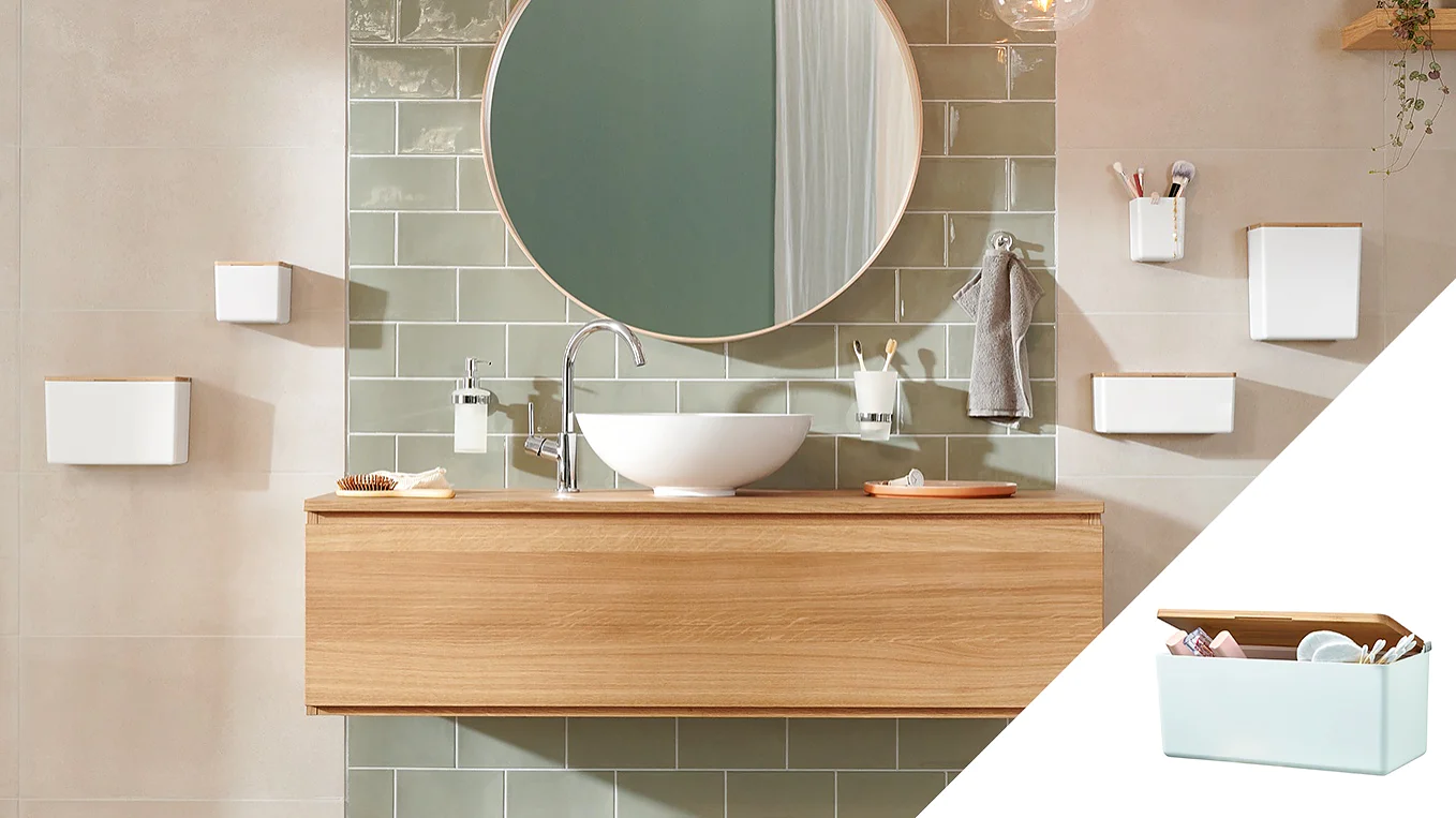 A modern bathroom features a wooden vanity with a white vessel sink, a round mirror, and green subway tiles. Various white wall-mounted accessories hold toiletries securely with tesa tape. An inset shows a white box with a wooden lid containing small items neatly held in place by tesa tape. (This text has been generated by AI)
