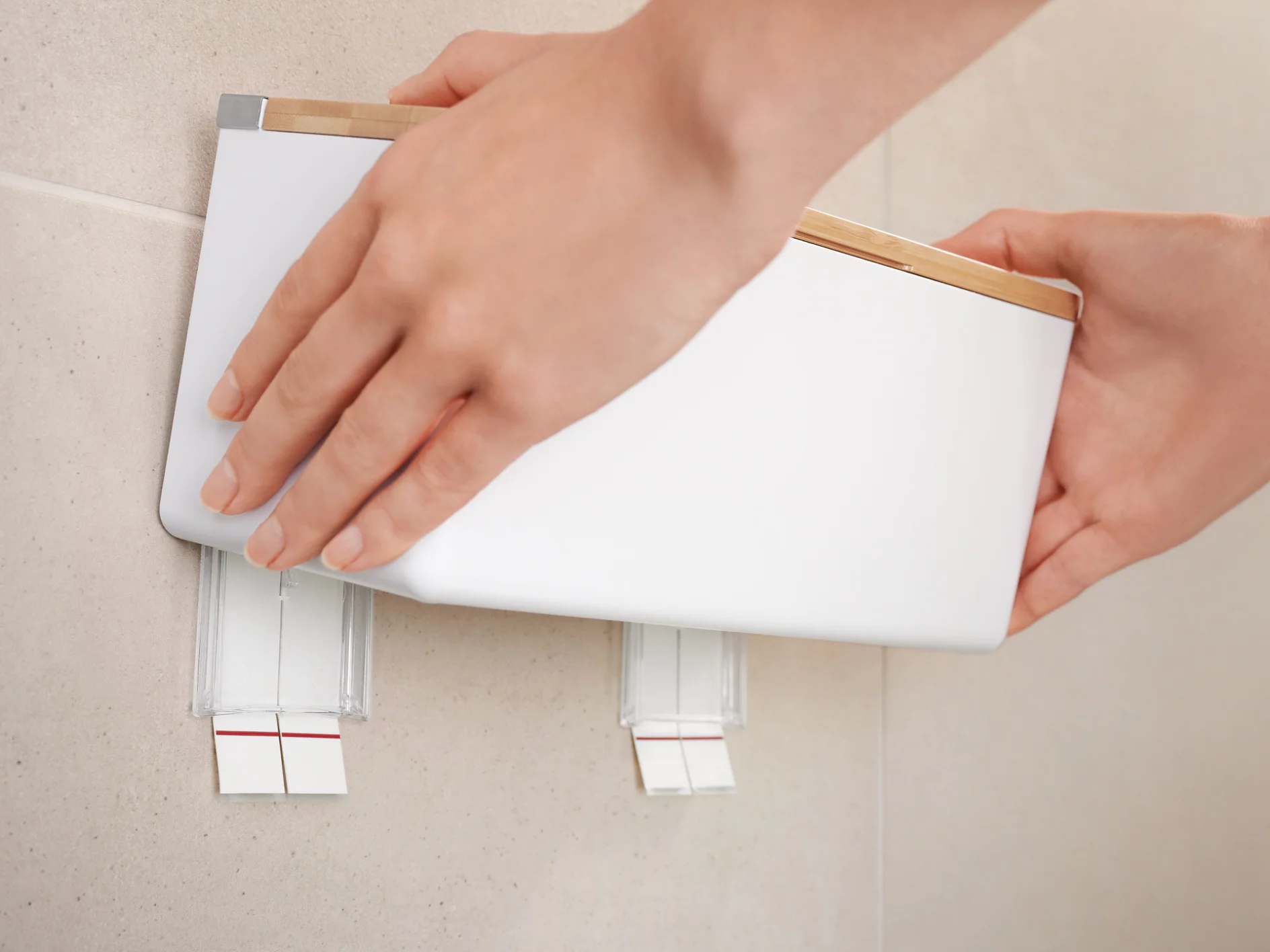 A person is mounting a white, rectangular device onto a wall using two tesa tape adhesive strips. The hands are adjusting the device to ensure it is level. The wall is light-colored, and the scene is indoors. (This text has been generated by AI)