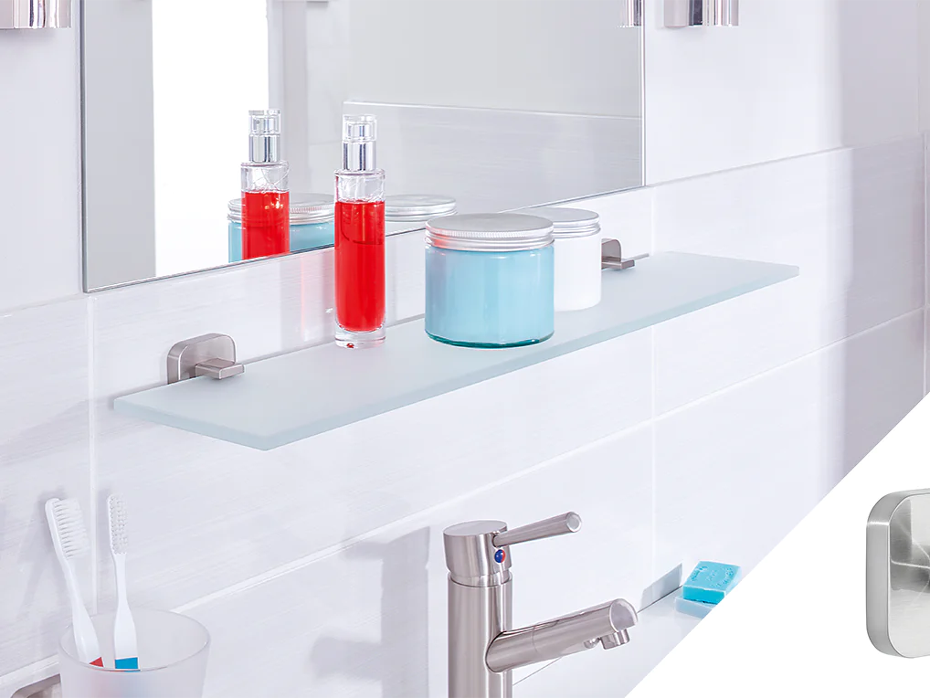 A modern bathroom counter with a glass shelf holding two bottles and a jar, one red and one blue. A mirror is above the shelf. Toothbrushes and a soap dispenser are on the counter. A small metallic wall hook, secured with tesa tape, is shown in a separate inset. (This text has been generated by AI)