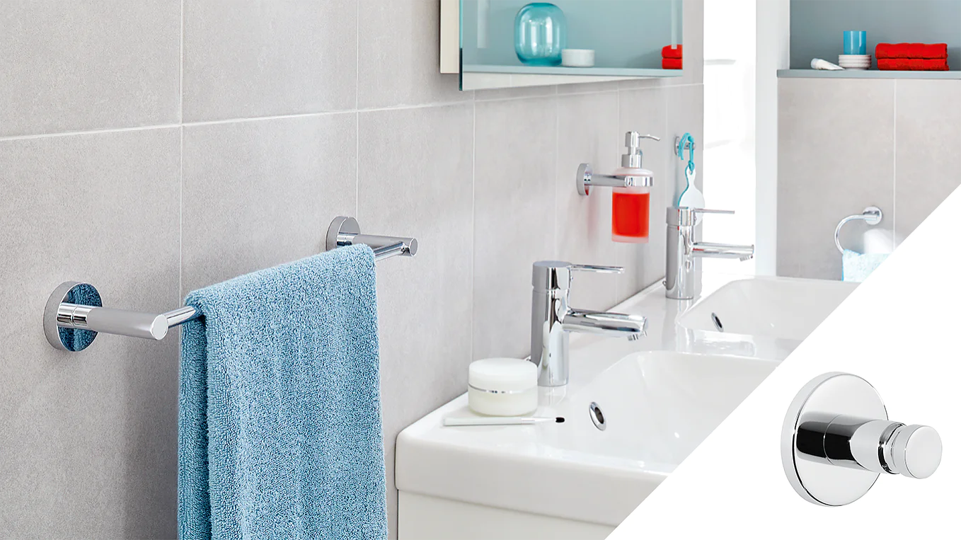 A modern bathroom features two white sinks with chrome faucets, a blue towel on a chrome towel bar, and a red liquid soap dispenser. The inset shows a close-up of a chrome wall hook attached with tesa tape on a light gray tiled wall. (This text has been generated by AI)