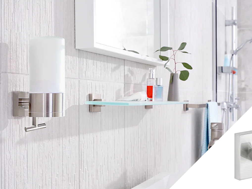 Wall-mounted bathroom accessories are shown, including a soap dispenser with a metal finish and a glass shelf holding a small bottle and a plant. A square wall hook is inset in the image, featuring a simple modern design, all secured using tesa tape. (This text has been generated by AI)