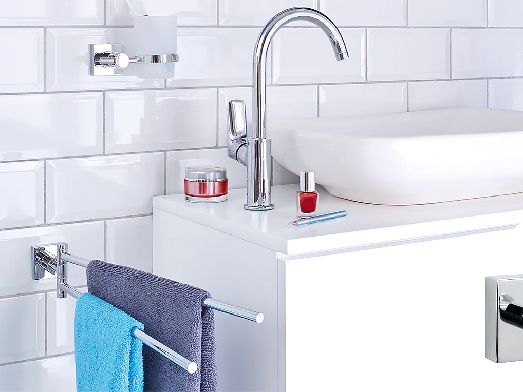 A modern bathroom counter with a white rectangular sink, chrome faucet, and accessories including red nail polish and cream jars. A blue towel hangs on a chrome bar. White subway tiles create the wall backdrop. A square hook is inset in the corner using tesa tape. (This text has been generated by AI)