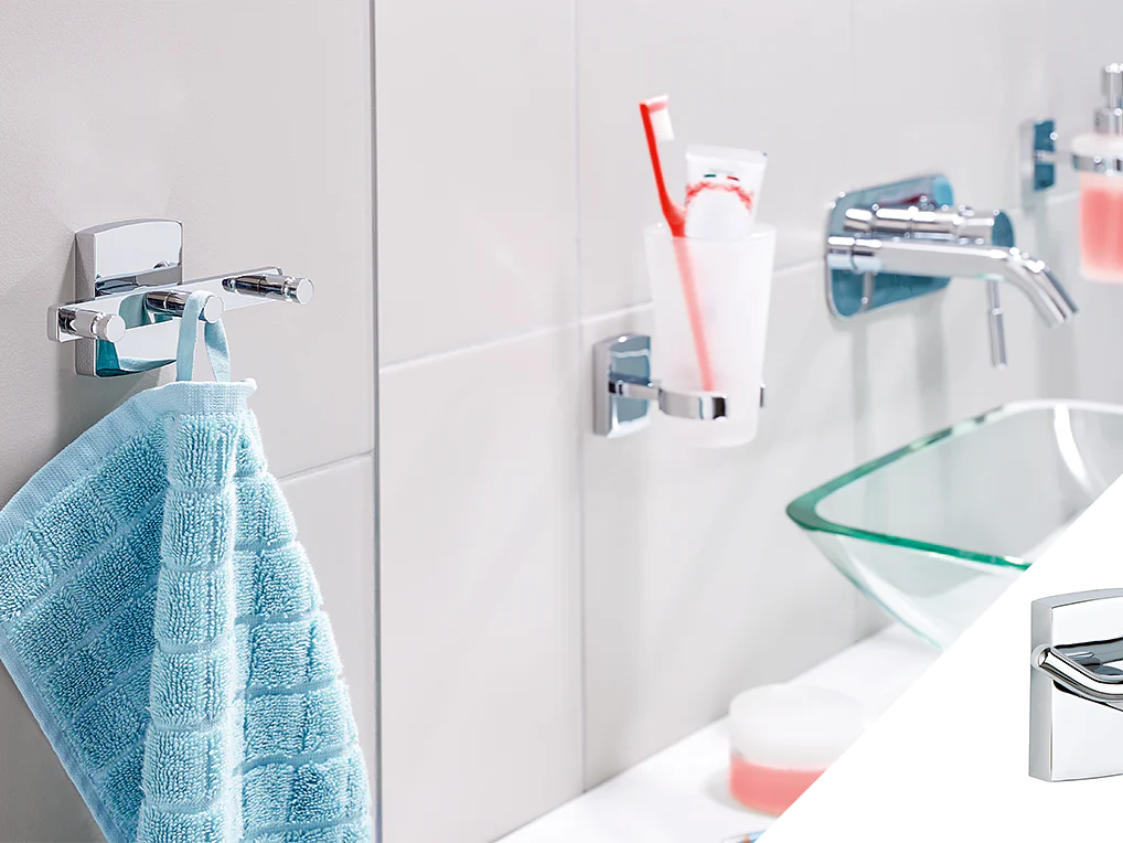 A modern bathroom setup with a light blue towel hanging on a chrome hook using tesa tape, a clear glass holding a red toothbrush above, and a soap dispenser on the right. The image also features a smaller inset of the chrome hook. (This text has been generated by AI)