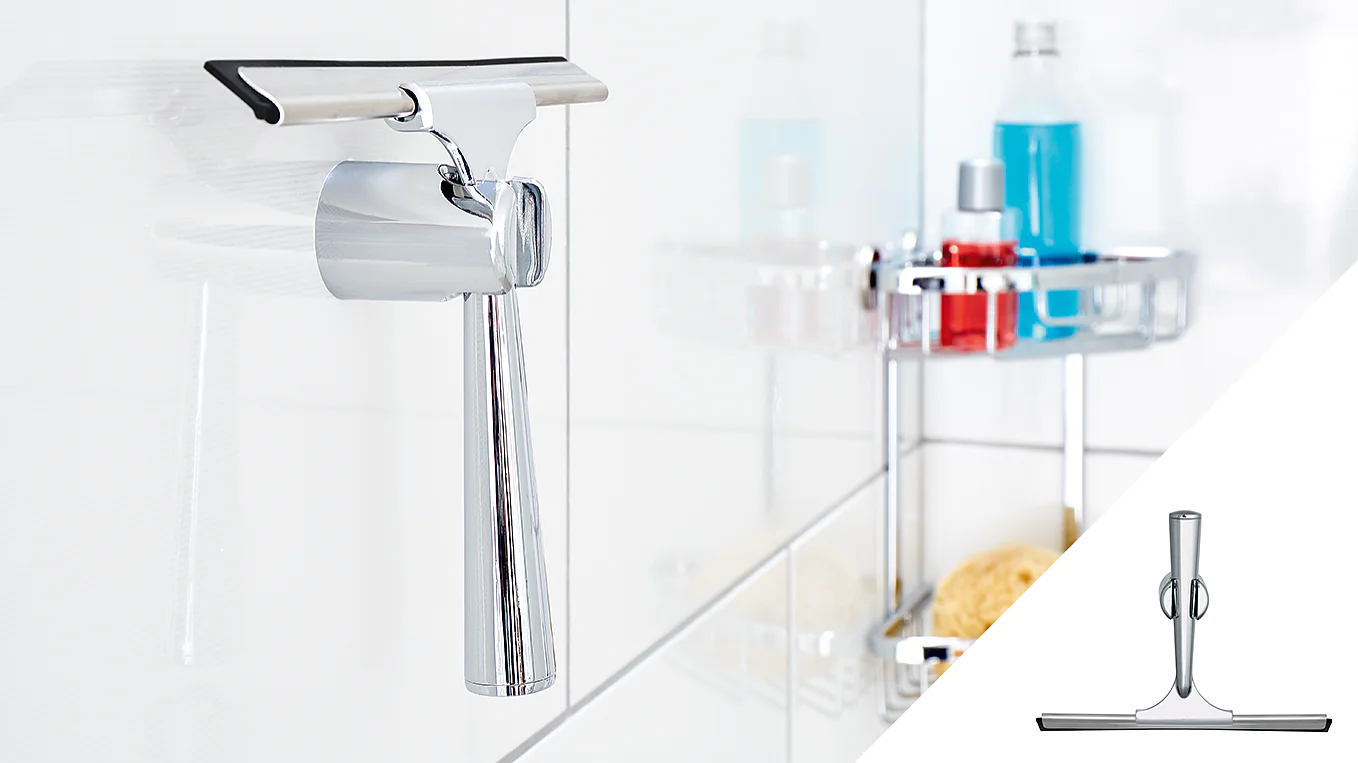 A metallic shower squeegee hangs on a hook attached to a tiled wall using tesa tape. In the background, a shower caddy holds various bottles and toiletries. An inset at the bottom right provides a close-up of the squeegee. (This text has been generated by AI)