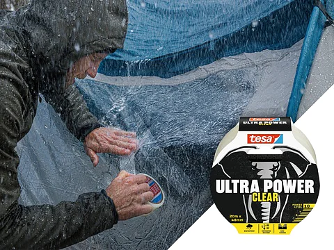 A person applies tesa Ultra Power Clear adhesive tape to a tent in heavy rain. The tesa tape packaging, featuring an image of an elephant and text tesa Ultra Power Clear, is displayed in the foreground. The tent is visibly wet from the rain. (This text has been generated by AI)