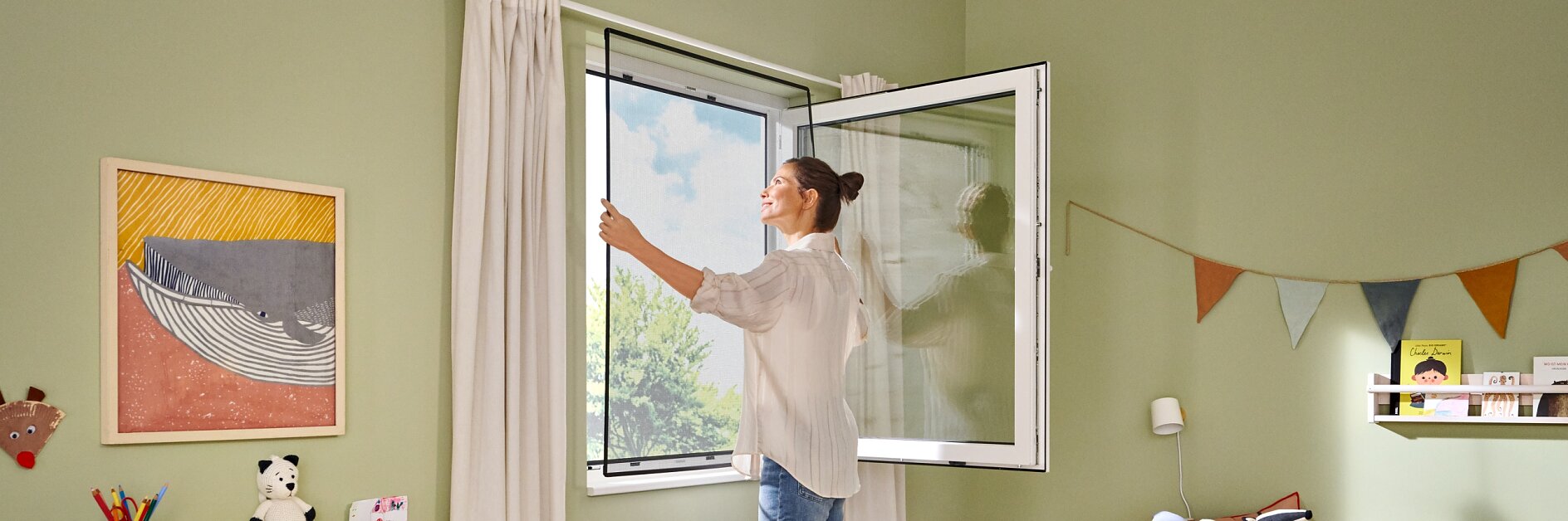 A woman opens a window in a childs room, which has green walls and wooden flooring. The room features a bed, a shelving unit with books and toys, a chair, and a wall decorated with bunting hung using tesa tape. Sunlight streams in, brightening the space. (This text has been generated by AI)