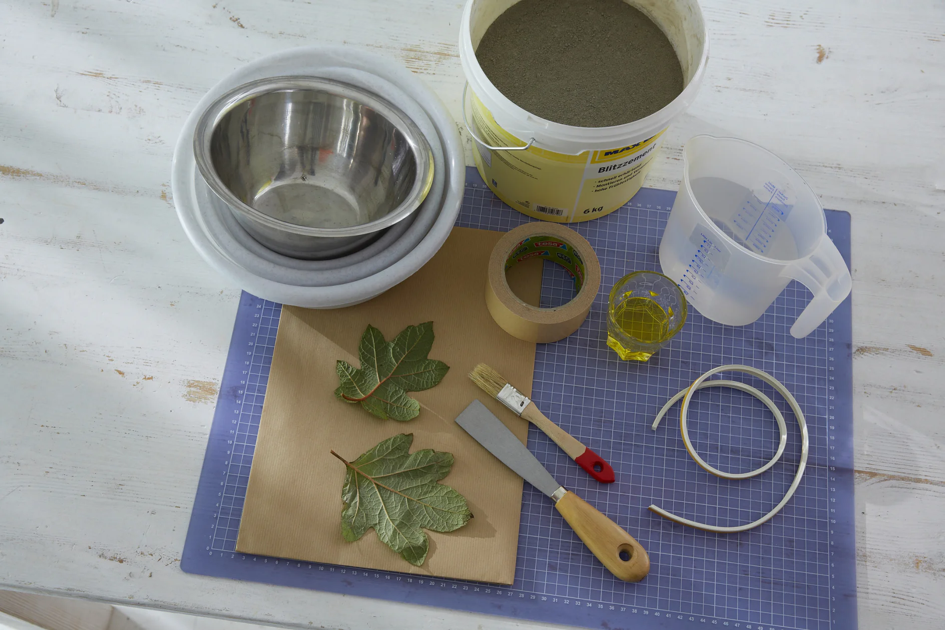 Das brauchen wir: Packpapier als Unterlage, Blitzbeton, Wasser, Speiseöl, Pinsel, Schüssel zum Anrühren des Blitzbetons, Spachtel zum Anrühren, Messbecher, 2 Schüsseln (eine größere und eine ca. 2 cm kleinere. Wichtig: Die kleinere Schale – sie gibt die innere Form – muss unten absolut glatt sein), frische Blätter mit schöner ausgeprägter Blattstruktur, tesa® Doppelseitiges Klebeband ECO FIXATION, tesamoll® E-Profil