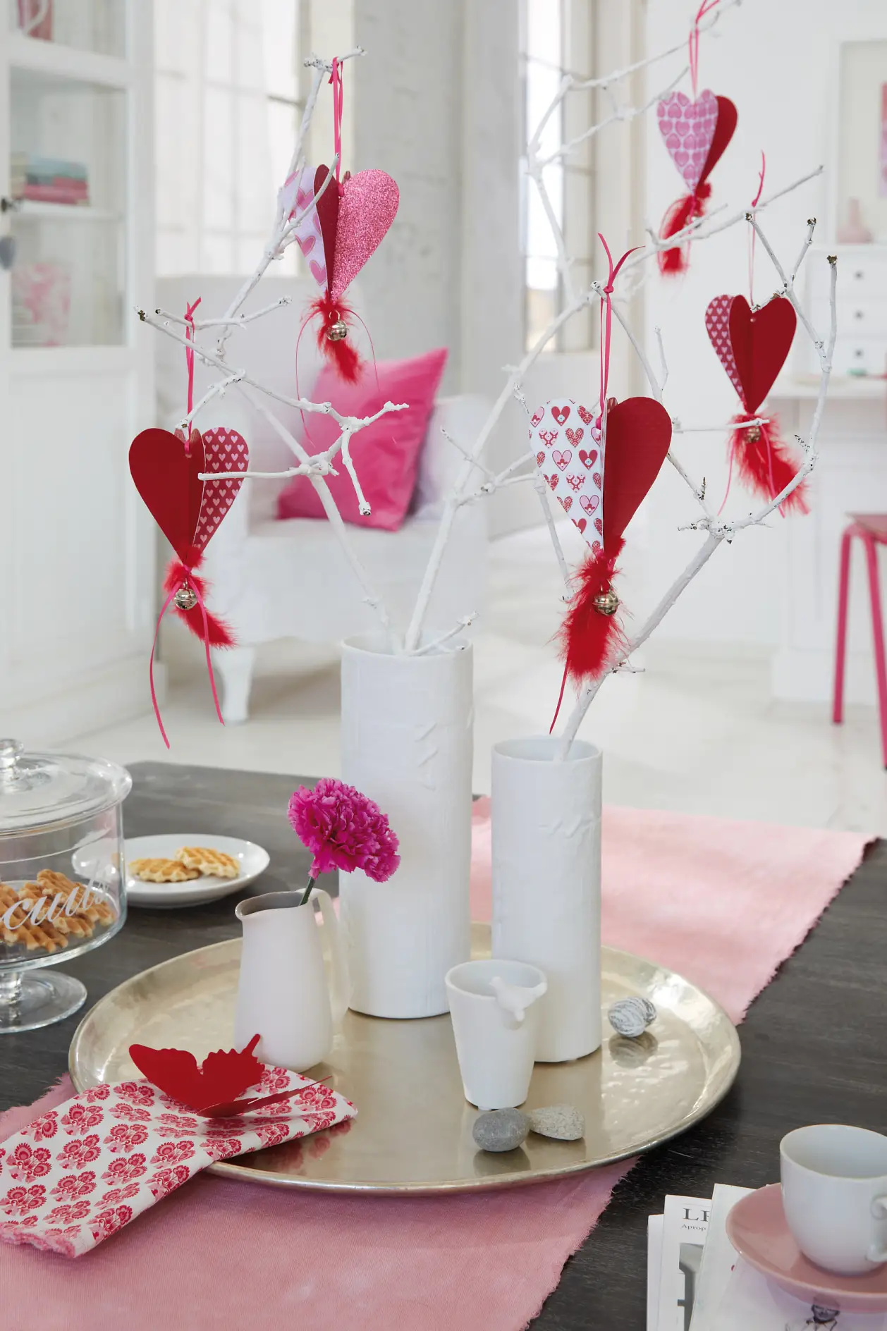 Selbstgemachte Papierherzen hängen zum Valentinstag in dem Strauß aus weiß lackierten Ästen.