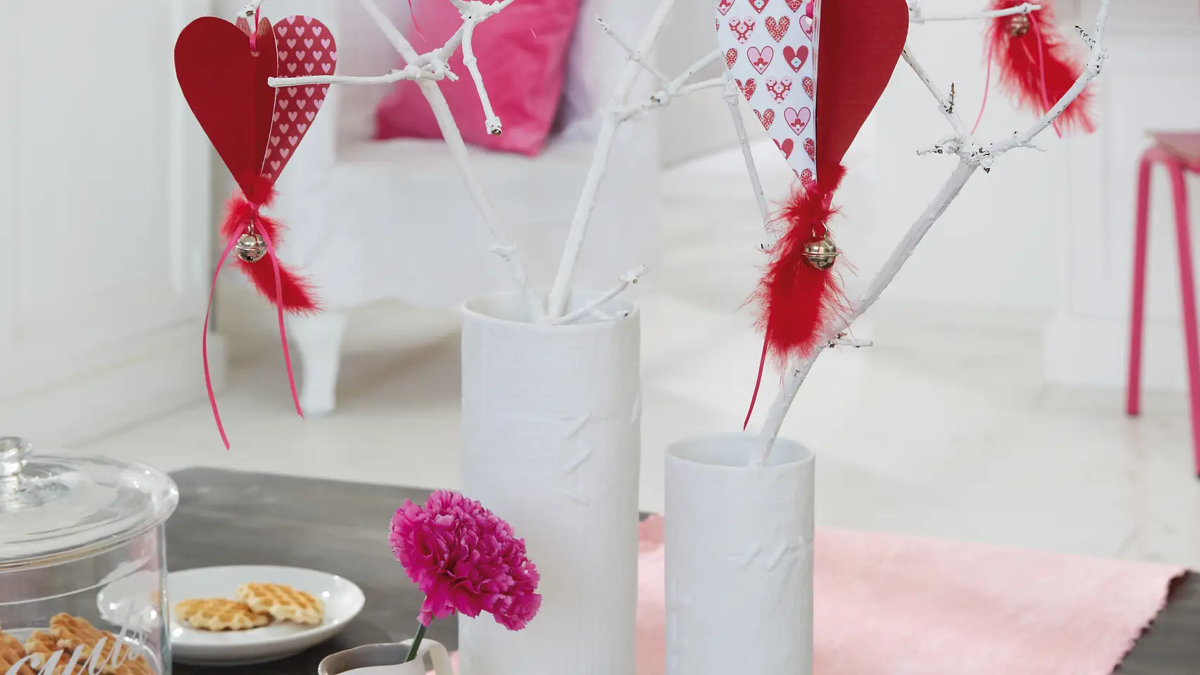 Selbstgemachte Papierherzen hängen zum Valentinstag in dem Strauß aus weiß lackierten Ästen.