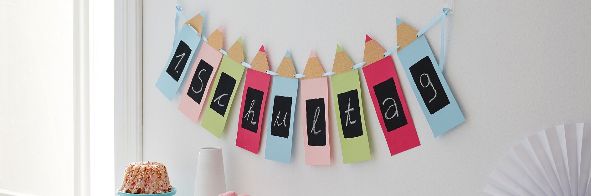 Kreidezeichen: An so einem besonderen Tag wird sogar die Wand geschmückt: Die Buntstiftgirlande zur Einschulung macht ganz unmissverständlich klar, was heute gefeiert wird! Sie ist schnell selbst gemacht und kann immer wieder neu beschriftet werden, weil die Schreibfläche ganz passend mit Tafellack angemalt ist.
