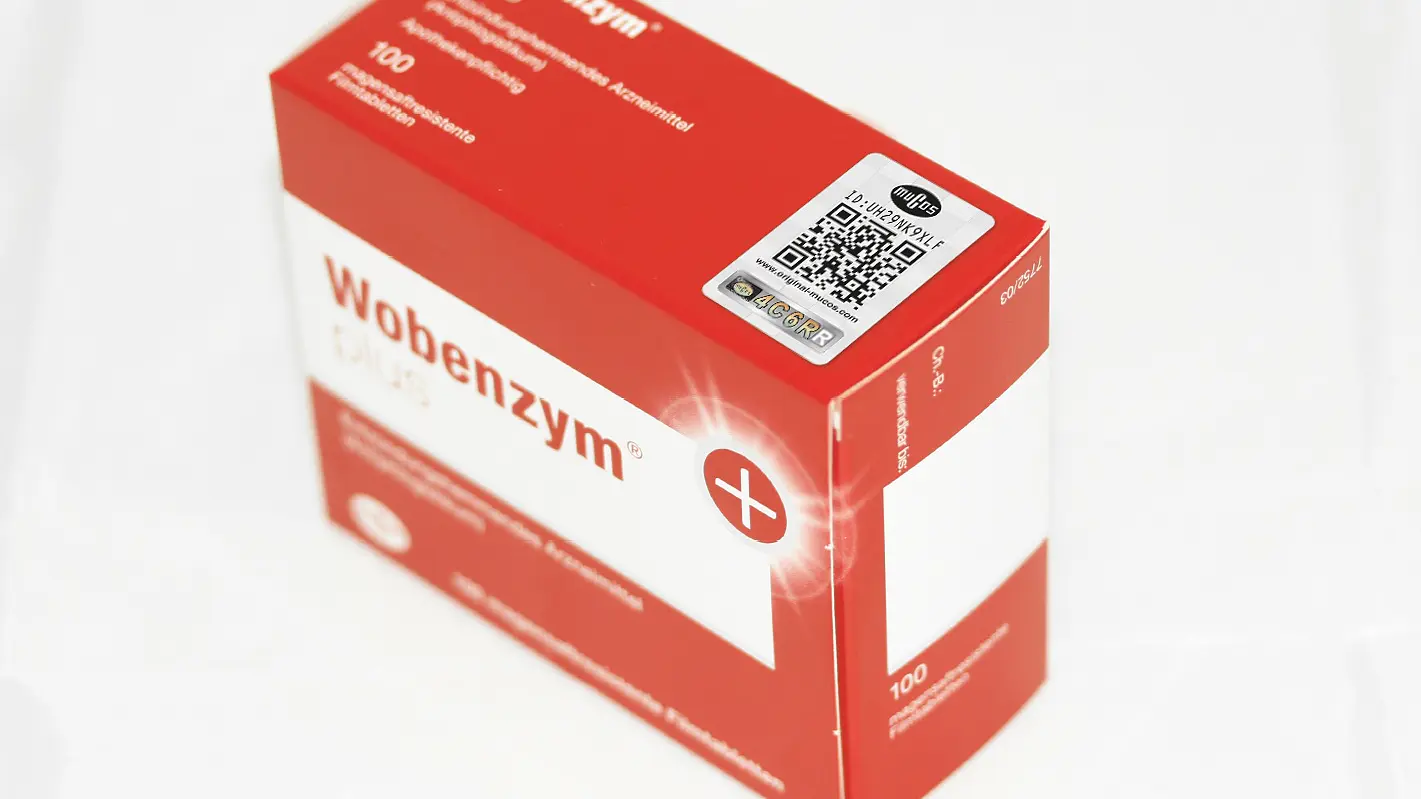 Zu sehen ist eine rote Schachtel mit der Aufschrift „Wobenzym Plus“. Sie trägt einen QR-Code und enthält, wie auf der Verpackung vermerkt, 100 magensaftresistente Tabletten.