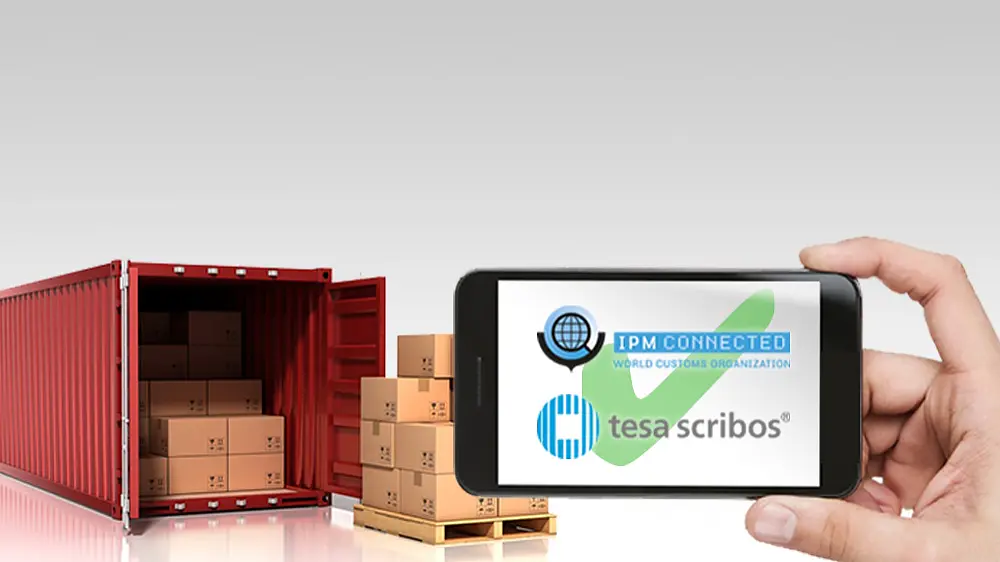 Eine Hand hält ein Smartphone, auf dem der Text „IPM Connected“ und „tesa scribos“ mit Logos angezeigt werden. Im Hintergrund sind ein roter Versandcontainer und Holzpaletten mit Kartons zu sehen. Das Setting suggeriert Logistik bzw. Sendungsverfolgung mittels Tesa-Klebeband.