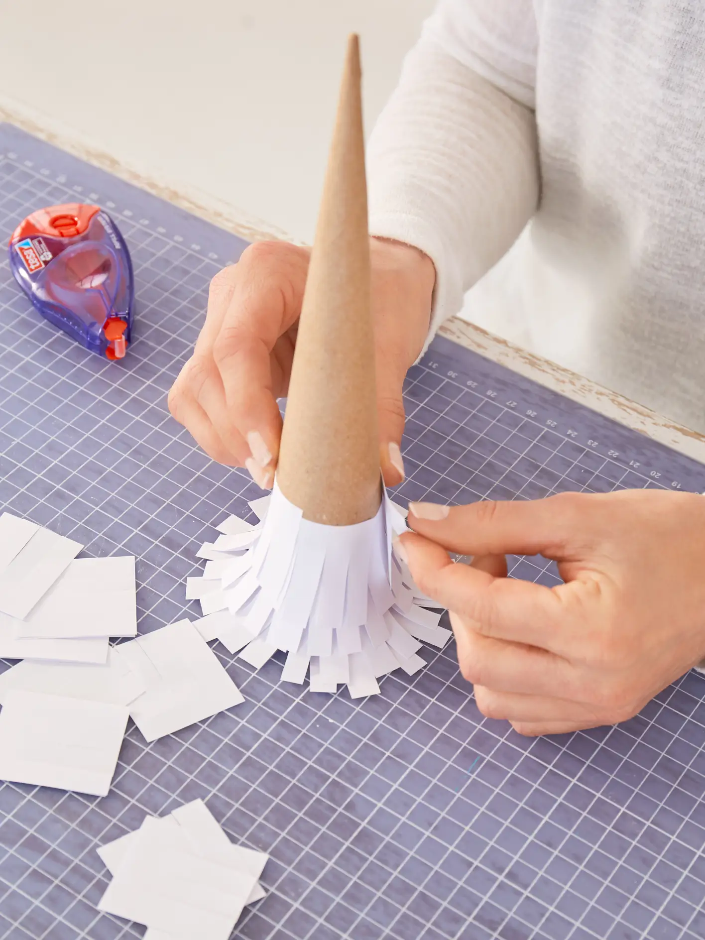 Die Papierstreifen und -kreise rundherum leicht versetzt auf die Pappkegel kleben.