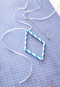 Von dem Band 1,5 m abschneiden und in die Nadel fädeln. Strohhalmstücke wie folgt auffädeln: ein langes, zwei kurze, ein langes. Band oben verknoten, dabei ein Stück von ca. 30 cm zum späteren Aufhängen berücksichtigen.