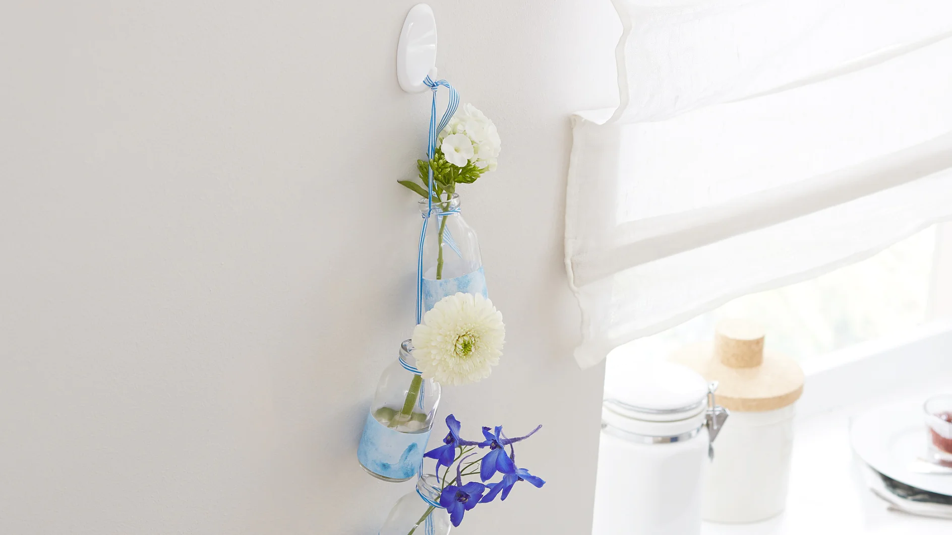 Jede Blume ist ein Kunstwerk – deshalb bekommt auch jede Blüte ihre eigene, individuell mit Papier verzierte Vase. Sie sind alle durch ein Band verbunden. Sicherer Aufhänger ist ein tesa Powerstrips® Haken LARGE Oval, der bis zu zwei Kilogramm tragen kann.
