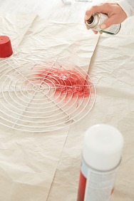 Die Füße der Gitter eventuell etwas nach innen biegen, damit sie gerade am Haken an der Wand hängen und nicht schief abstehen. Gitter weiß grundieren und nach dem Trocknen partiell mit der roten Farbe besprühen.