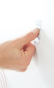 Powerstrip® mindestens fünf Sekunden lang fest auf die gewünschte Stelle an der Wand drücken. Darauf achten, dass die rote Linie des Powerstrips® unten ist. Die Schutzfolie am Anfasser nicht entfernen.