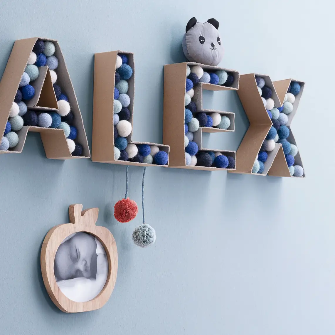 3D-Buchstaben aus Karton gefüllt mit bunten Filzkugeln, die den Namen „Alex“ schreiben.